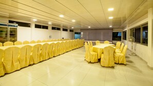 Una sala de conferencias con largas mesas y sillas, un refrigerador y un ventilador.
