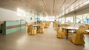 Un amplio espacio interior con varias mesas y sillas, una recepción y grandes ventanales que dejan entrar luz natural.