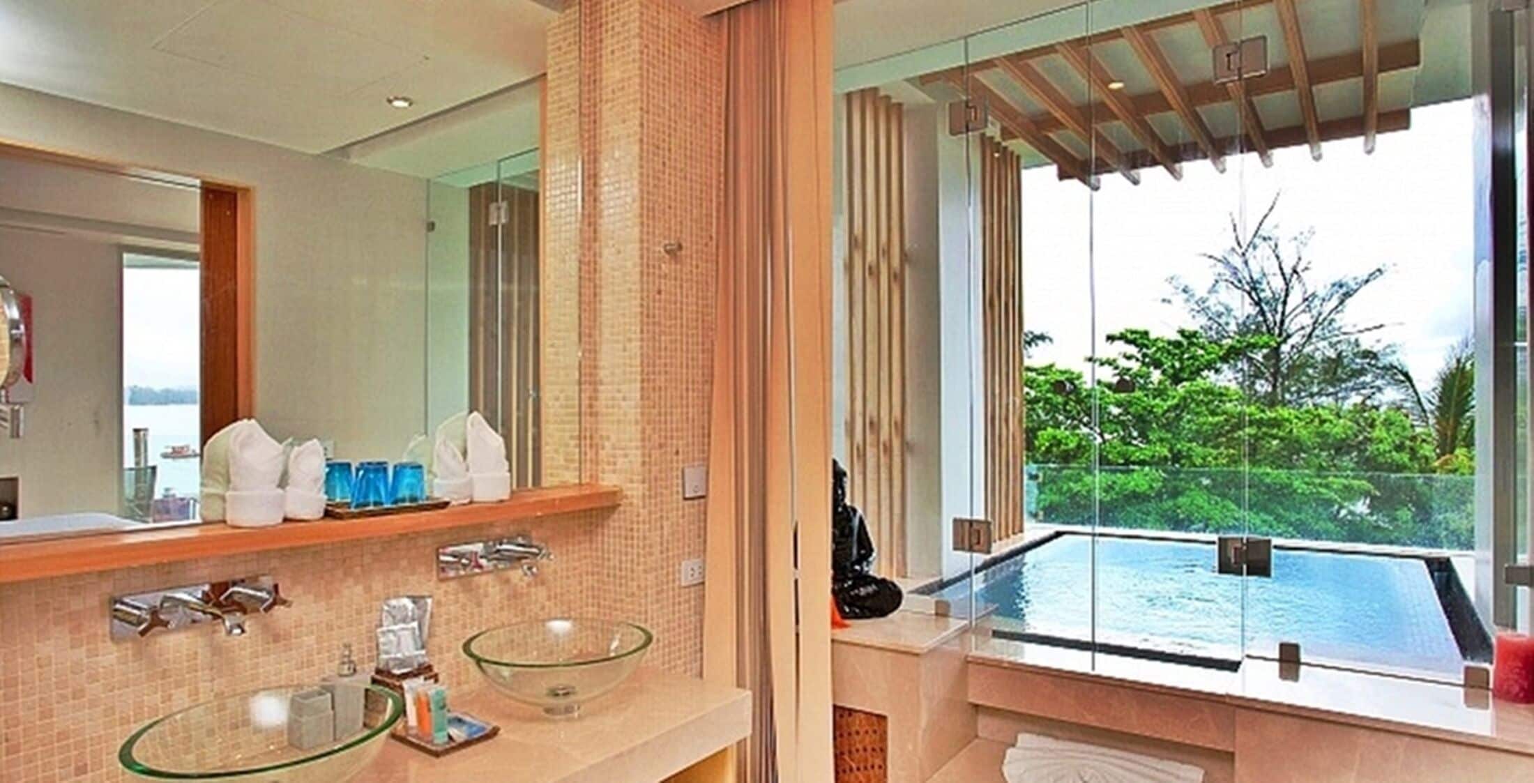 A modern bathroom with a glass-enclosed infinity pool, a large mirror, and a view of lush greenery.