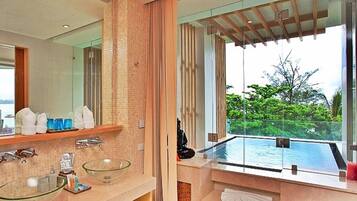 A modern bathroom with a glass-enclosed infinity pool, a large mirror, and a view of lush greenery.