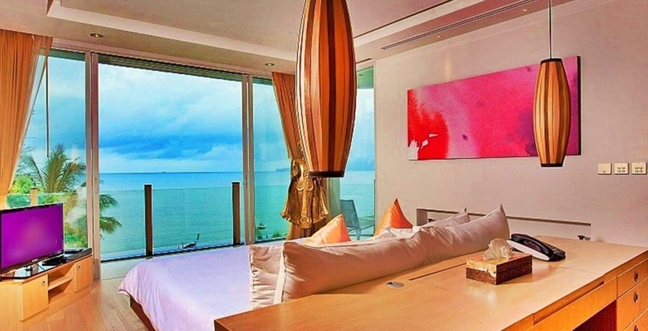 A hotel room with a bed, a desk, a TV, and a large window with a view of the ocean.