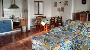 Une cuisine équipée d’une cuisinière, d’un four et d’un évier, une table à manger avec des chaises, un canapé à motifs et une horloge murale.