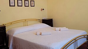 Una cama bien hecha con sábanas blancas y un cabecero dorado, una araña y tres cuadros en la pared.
