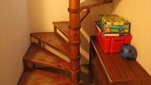 Un escalier en colimaçon en bois, avec une boîte de rangement rouge et une balle bleue sur le palier.