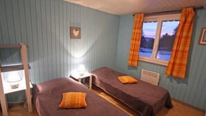 Une chambre avec deux lits simples, un bureau avec une lampe, une fenêtre avec des rideaux et un décor en forme de cœur fixé au mur.