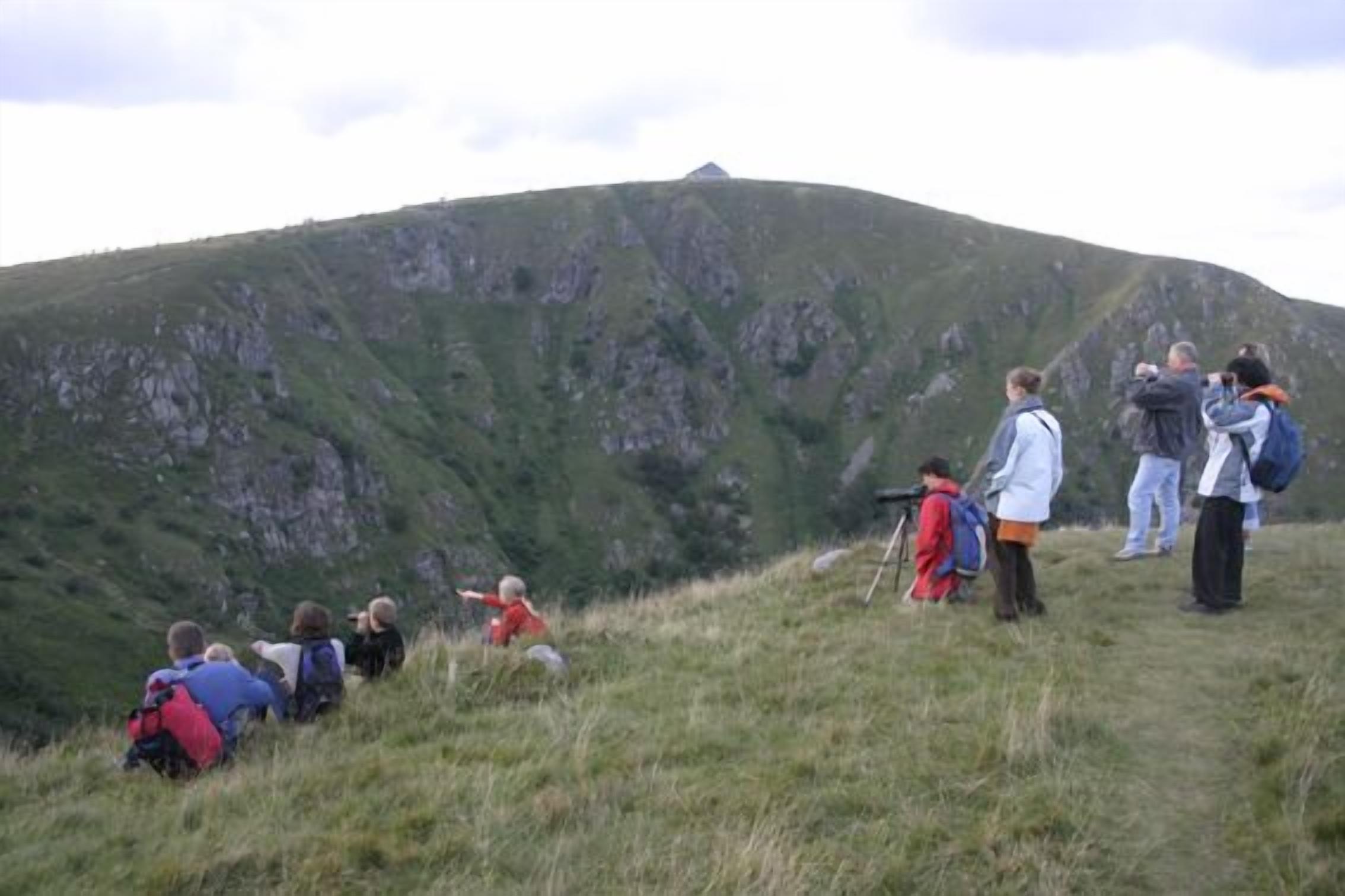A group of people hiking on a grassy hill with a rocky mountain in the background.