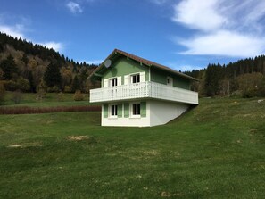 A two-story house with a balcony, surrounded by a grassy field and forested hills. - Mountain chalet in La Bresse Htes Vosges label "Family Plus", Gîte de France (La Bresse)