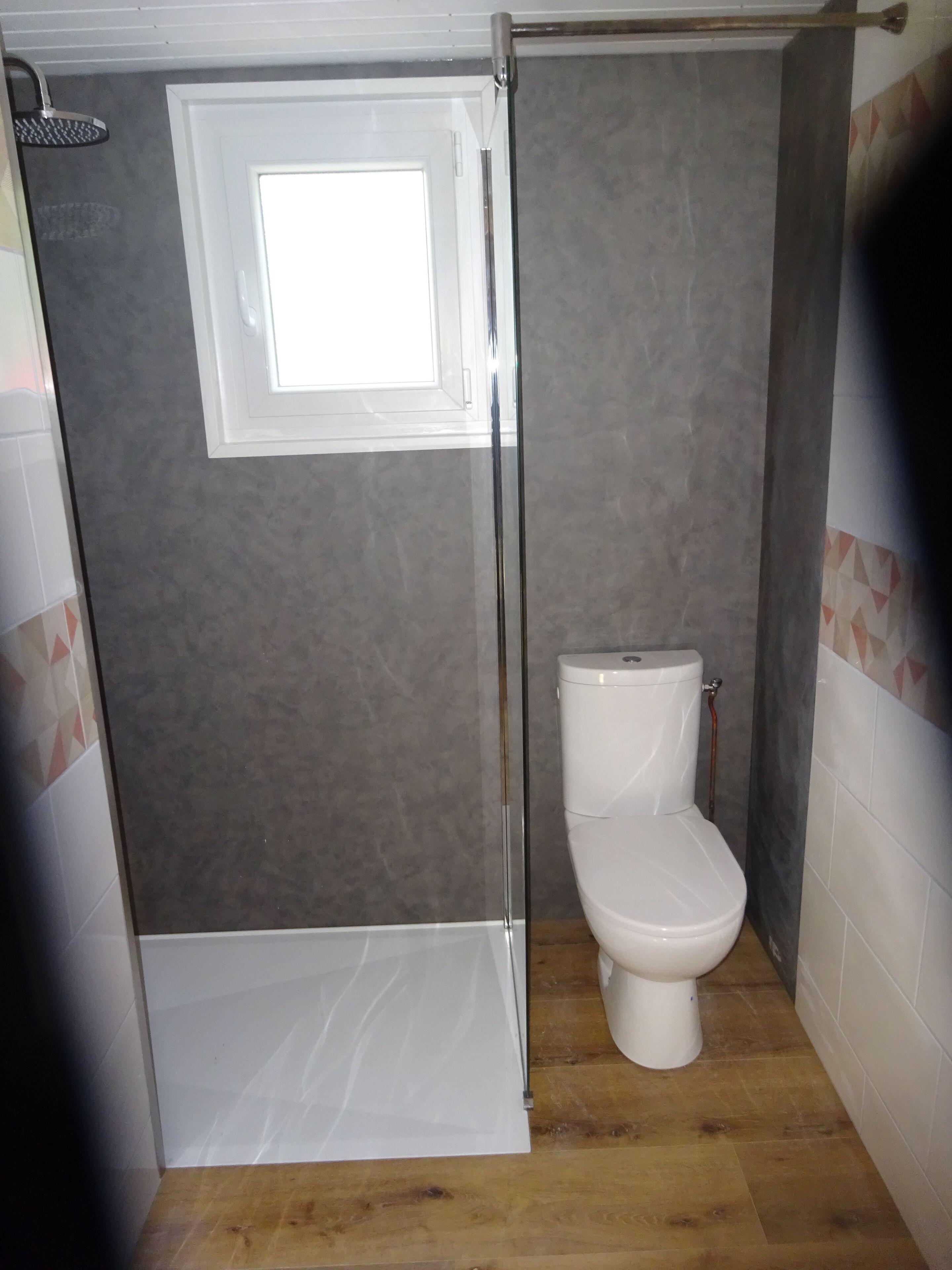 A bathroom with a shower enclosure, a toilet, and a window.