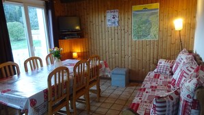 Une pièce chaleureuse avec un décor intérieur en bois, une table à manger avec des chaises, un canapé, un téléviseur et une lampe.