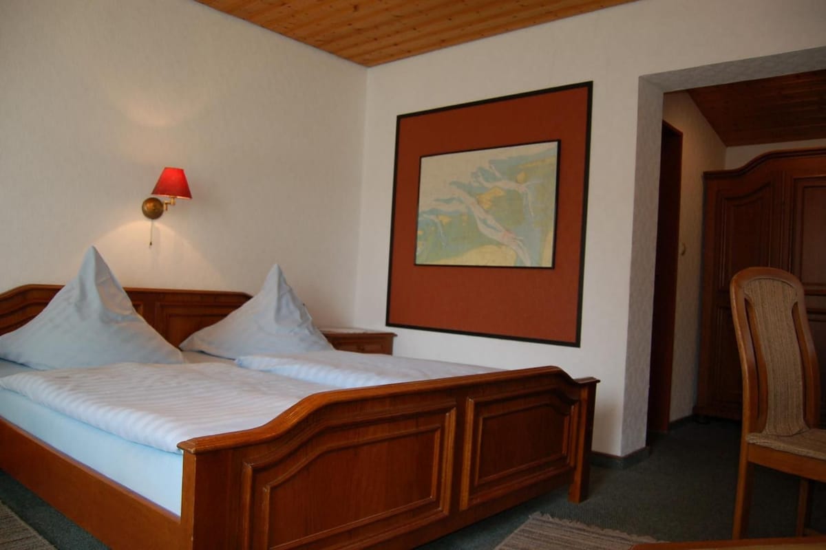 A bedroom with a wooden bed, a nightstand, a wall-mounted lamp, and a framed picture.