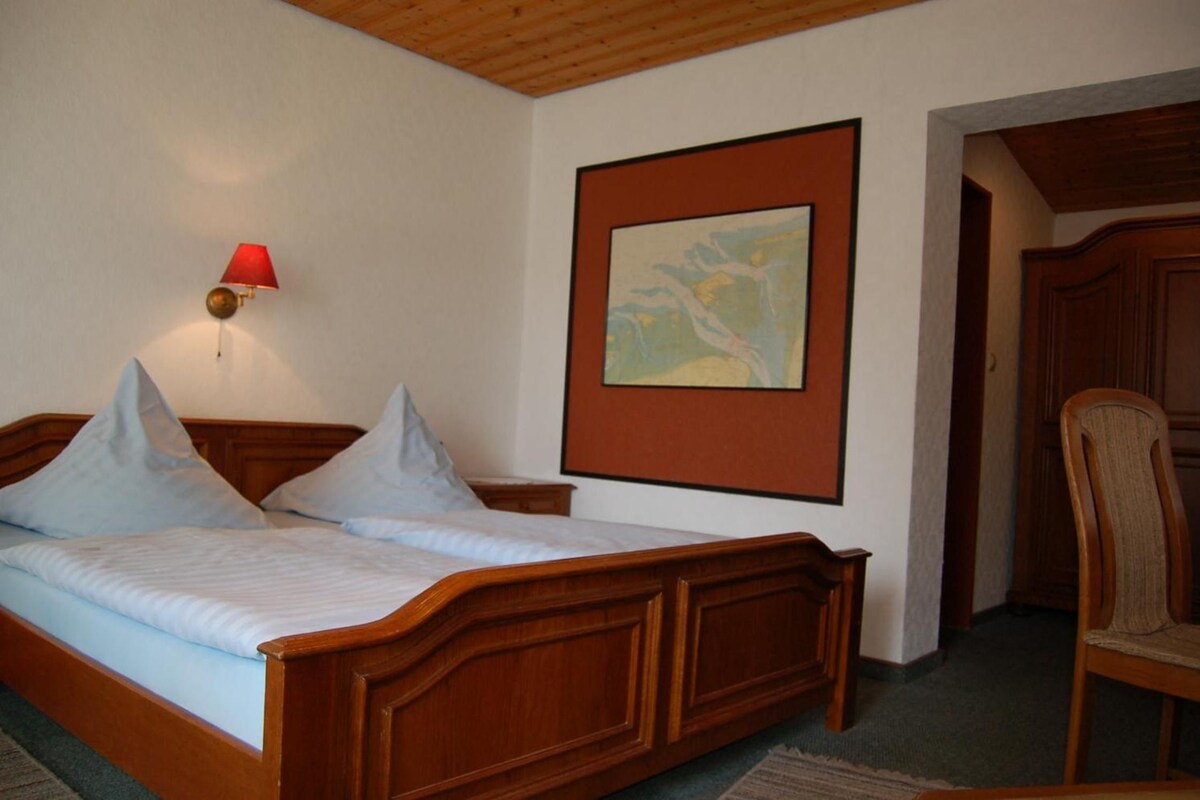 Un dormitorio con cama de madera, mesita de noche, lámpara de pared y un cuadro enmarcado.