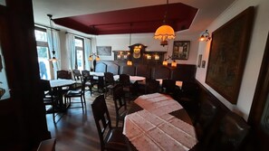 A dining area with multiple tables and chairs, a red ceiling, and pendant lighting.