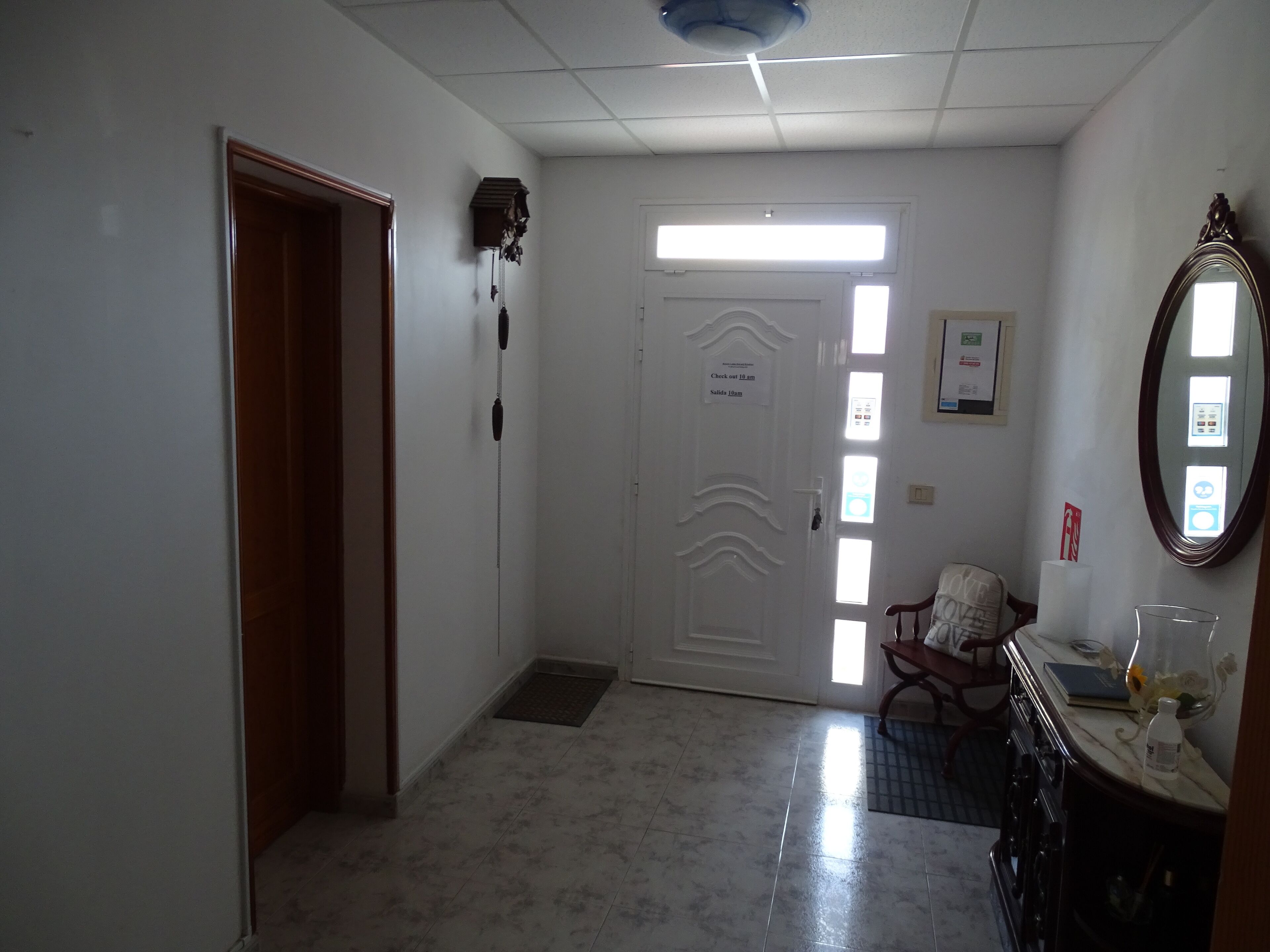 Un pasillo con una puerta blanca, un letrero de recepción, un espejo y una zona de lavamanos.