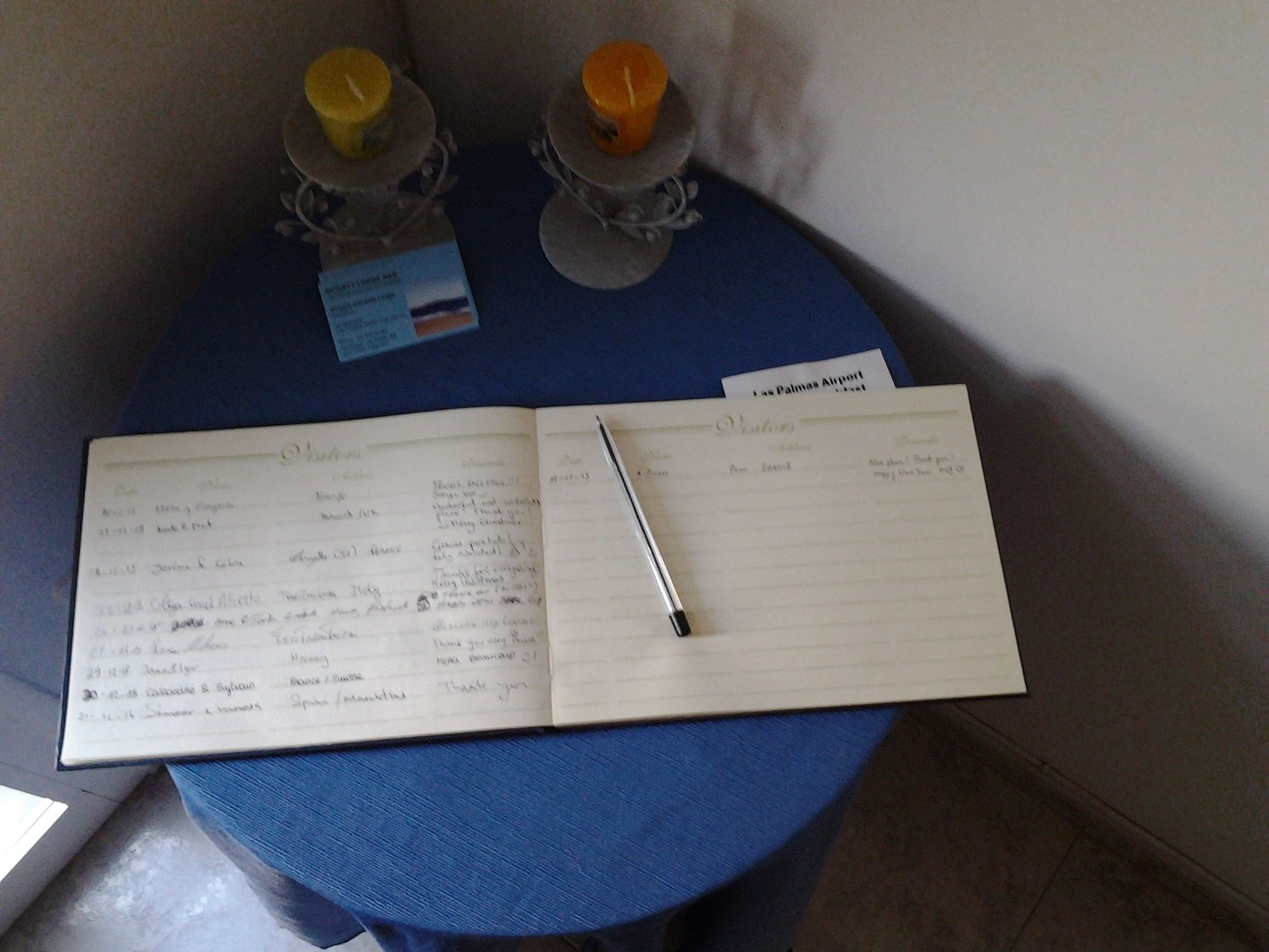 Un quaderno su un tavolo blu con due candele, un biglietto e una penna.
