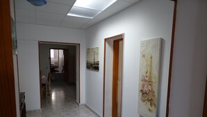 Un pasillo con suelo de baldosas, una mesa azul y una puerta que da a otra habitación.