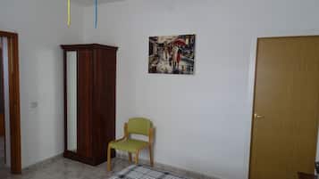 A bedroom with a bed, a wooden wardrobe, a green chair, a door, and a wall-mounted painting.