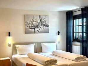 A hotel room with a bed, a wall-mounted artwork, and a window with curtains.