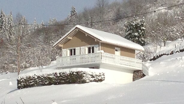 Een huis bedekt met sneeuw, met een balkon, omringd door bomen en een besneeuwd landschap.