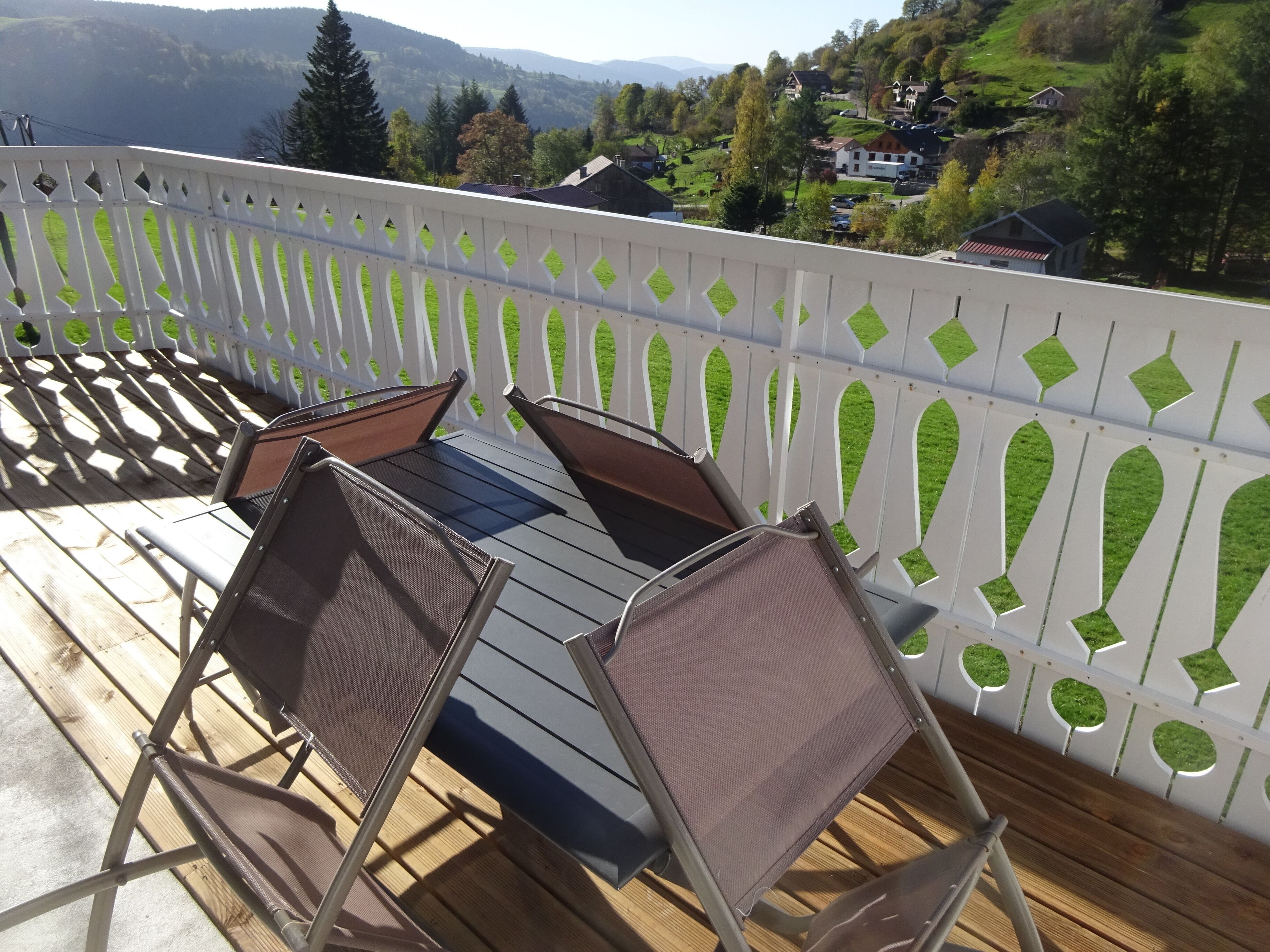 A balcony with a table and chairs, overlooking a scenic landscape with houses and trees.