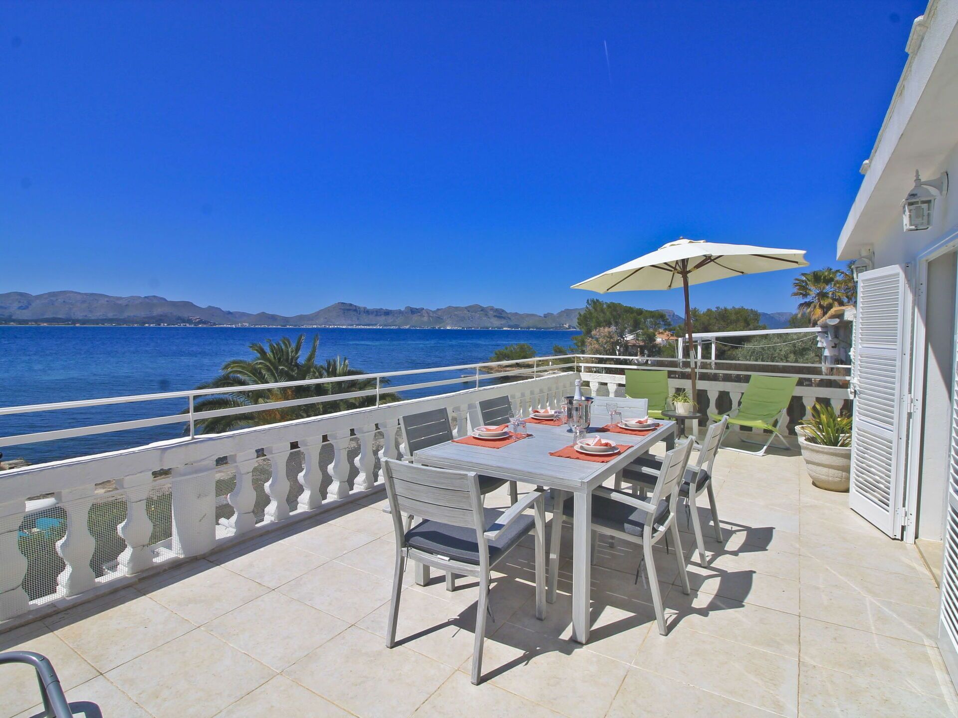 A terrace with a table set for dining, overlooking a body of water and mountains.