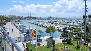A marina with numerous boats docked, a promenade with palm trees, and a clear sky. - Beautiful apartment for 4 guests with A/C, WIFI, TV and patio (Alcúdia)