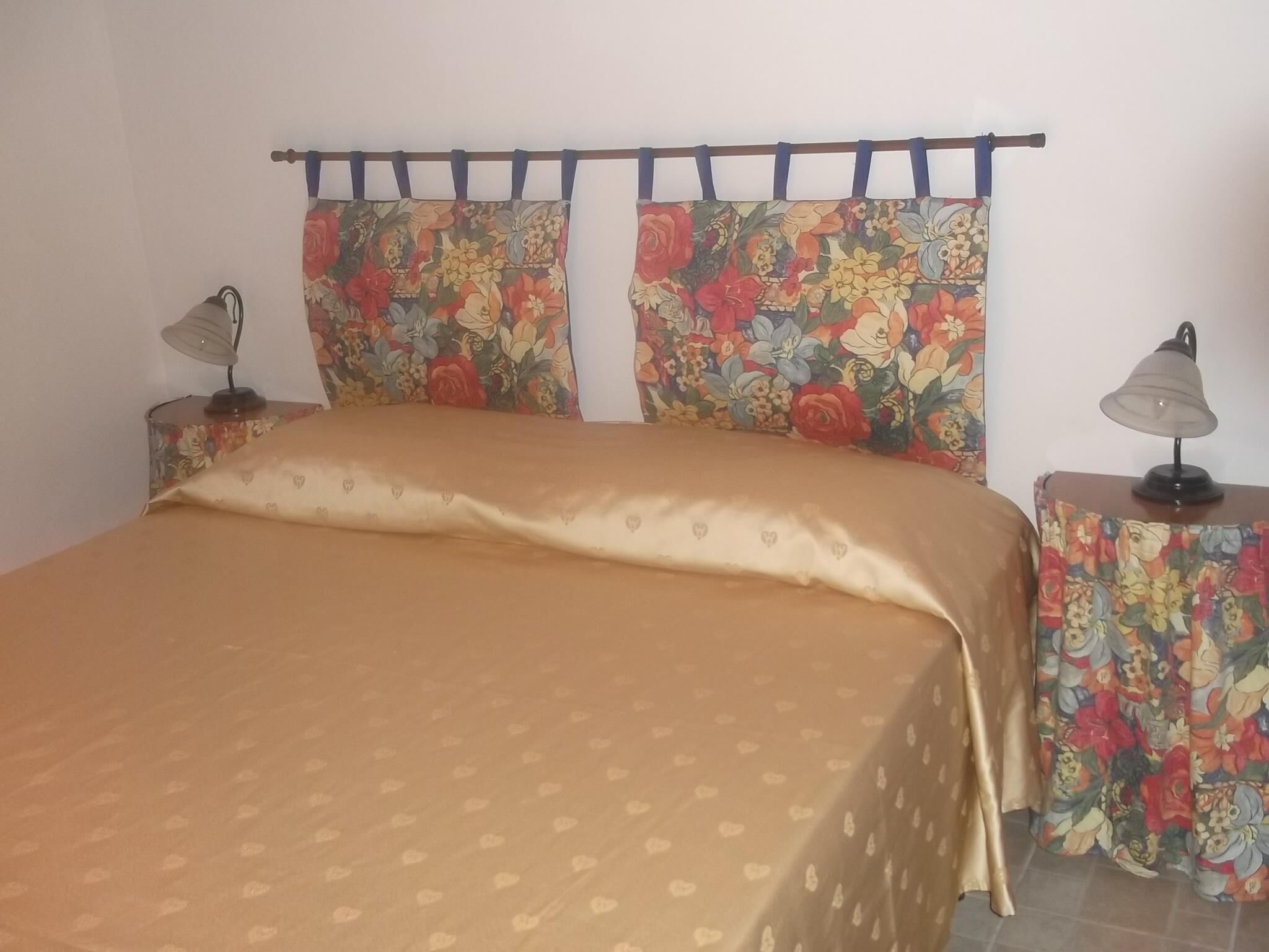 A bed with a floral-patterned headboard and curtains, flanked by two nightstands with lamps.
