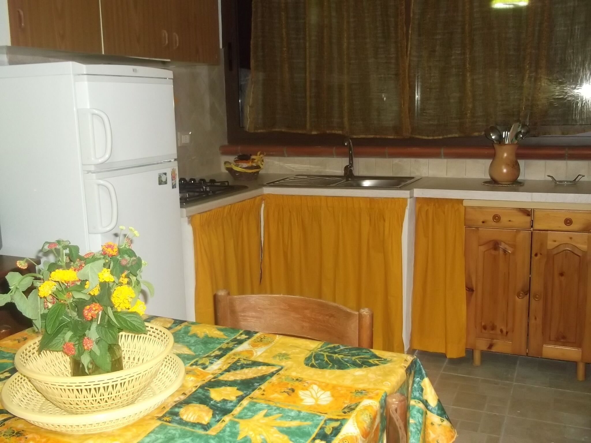 Una cucina compatta con frigorifero, lavello, mobili in legno e un tavolo con tovaglia floreale.