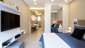 Ein modernes Hotelzimmer mit einem großen Flachbildfernseher, einem Bett mit blauer und weißer Bettdecke, einem Nachttisch mit Lampen und einem Spiegel.