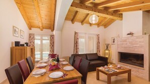 A dining area with a wooden table set for four, surrounded by leather chairs. A fireplace is visible in the background, and a sofa is placed against the wall.