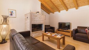 A cozy living room with a stone fireplace, leather sofas, a wooden coffee table, and a television.