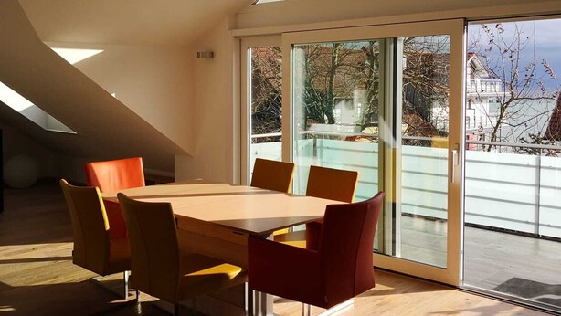 A modern dining area with a large table and chairs, large windows, and a sloped ceiling. - Fantastic, exclusive apartment with fantastic lake and alpine views (Immenstaad am Bodensee)