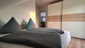 A bedroom with a bed, pillows, a wardrobe, and a view through a window. - Fantastic, exclusive apartment with fantastic lake and alpine views (Immenstaad am Bodensee)
