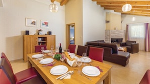 A dining area with a wooden table set for four, red chairs, and a wooden buffet cabinet. There is a fireplace in the background and a living area with a sofa and a coffee table. - Quiet holiday house with large pool on the outskirts of Rezanci (Rezanci)