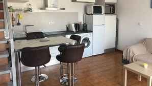 A compact kitchen with a washing machine, a microwave, and a coffee maker. There is a dining area with a table and bar stools. - House on port with garden-Mooring possible-Santa Margarida Rosas (Roses)