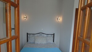 Un dormitorio con cama, ventanas con marco de madera y luces fijadas a la pared.