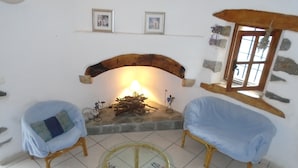 Una sala de estar acogedora con chimenea, dos sillones, una mesa de centro de vidrio y una alfombra colorida.