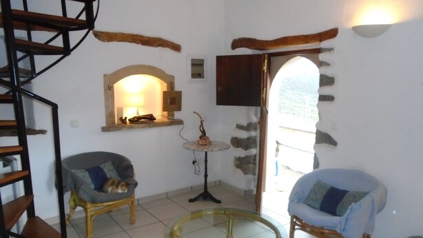 Una sala de estar acogedora con una escalera espiral, dos sillones de mimbre, una mesa de centro de vidrio y una pared de piedra.