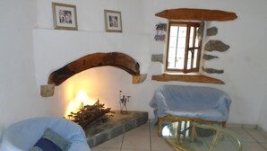 Una sala de estar acogedora con una chimenea de piedra, una mesa de centro de vidrio, un sofá azul y una silla de mimbre.