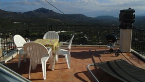 Una terraza con mesa y sillas, una parrilla de barbacoa y vistas a las montañas.