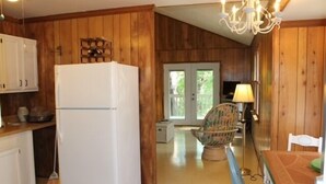 A kitchen with wooden walls, a white refrigerator, and a dining area with a table and chair. - Treehouse OBX. Cozy cottage in family/pet-friendly neighborhood. Close to sound. (Kill Devil Hills)