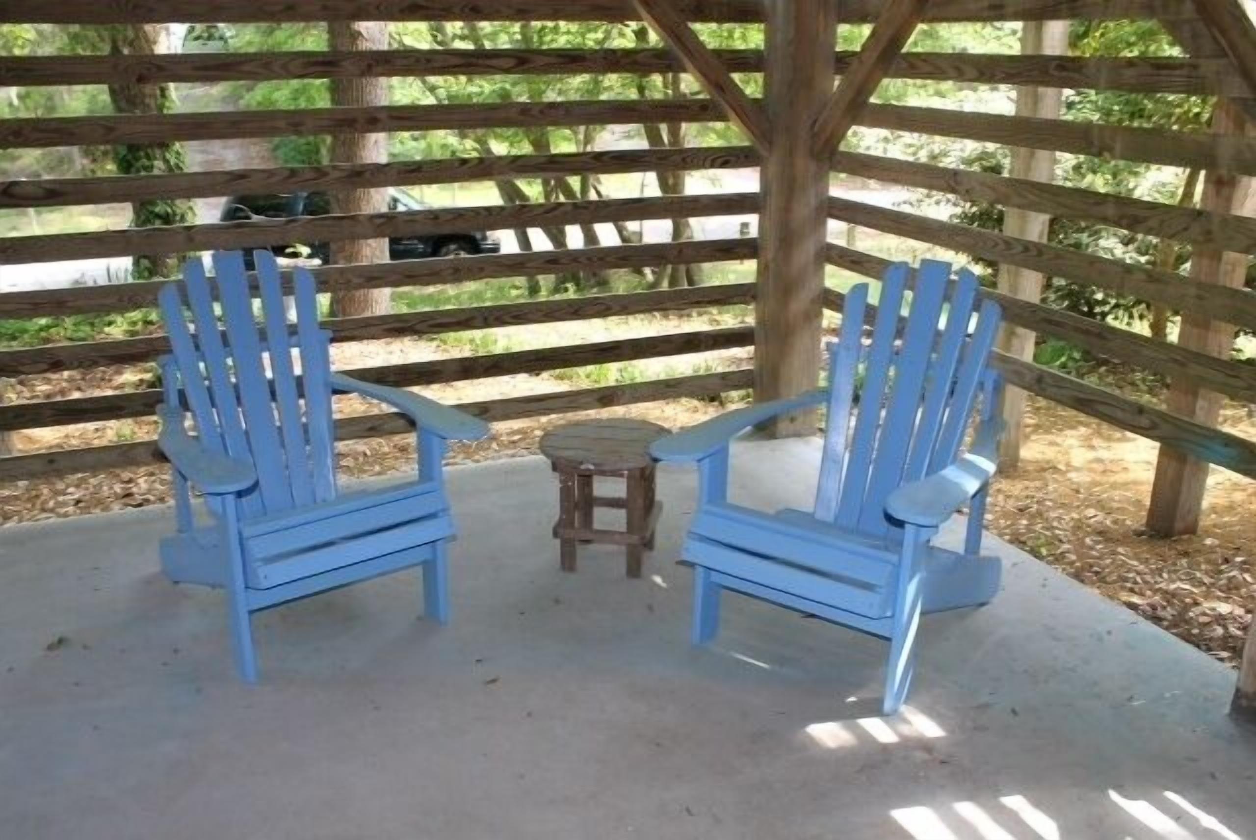 Two blue Adirondack chairs and a small wooden table under a wooden pergola.
