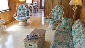 A cozy room with two floral-patterned armchairs, a matching sofa, and a small side table with a book. - Treehouse OBX. Cozy cottage in family/pet-friendly neighborhood. Close to sound. (Kill Devil Hills)