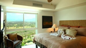 Un dormitorio con cama, una silla, un ventilador de techo, una ventana con vistas y un cuadro en la pared.