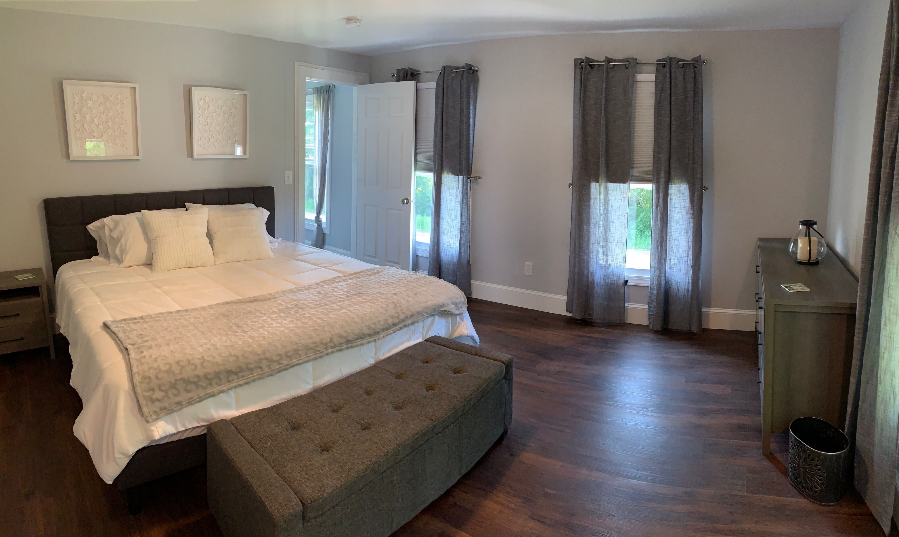 A bedroom with a large bed, a bench, two framed artworks, and a nightstand.