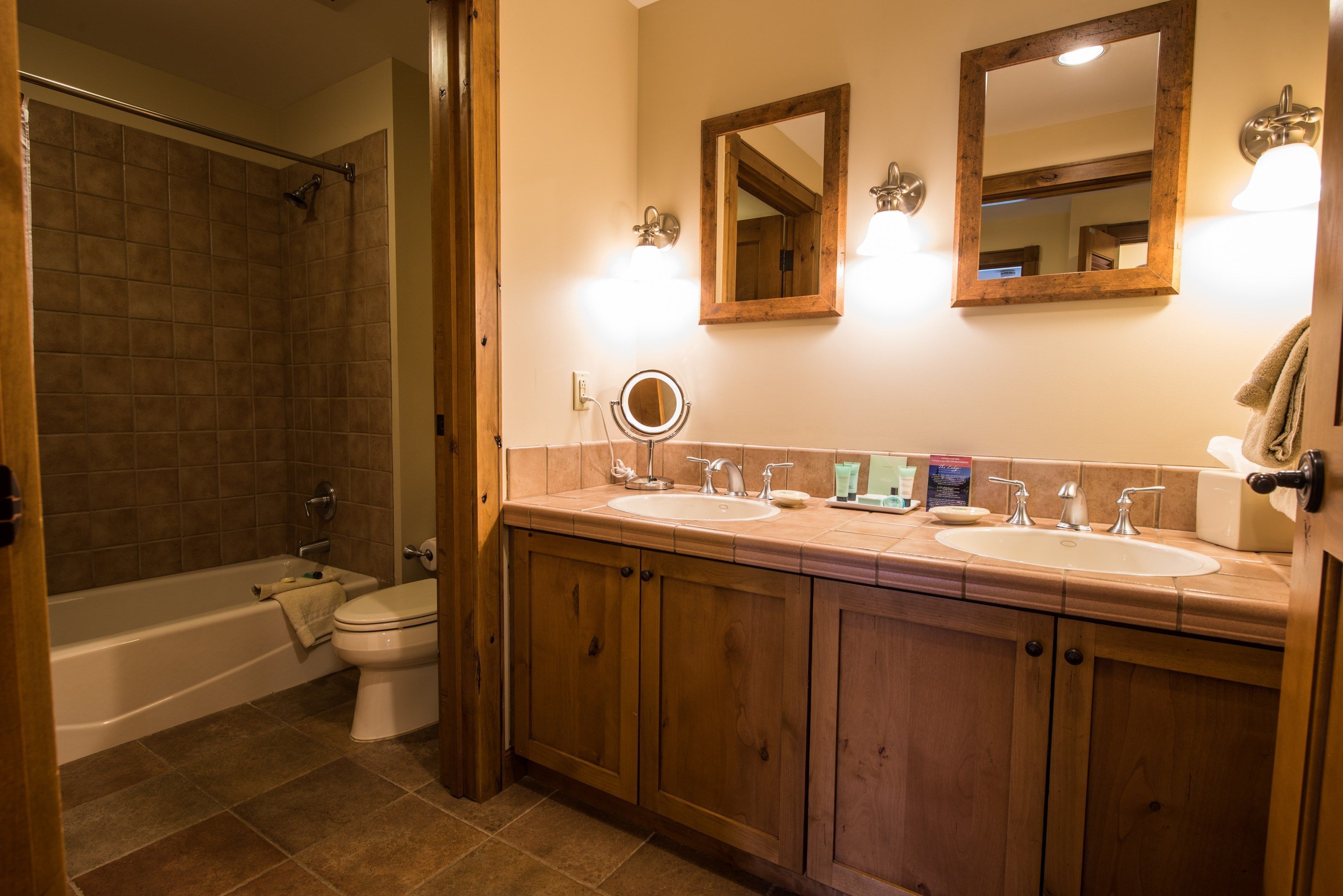 Une salle de bain avec deux lavabos, des toilettes, une douche, des meubles en bois et un miroir.