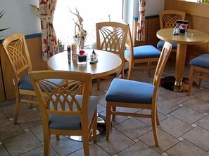 A dining area with wooden chairs and a round table, featuring a blue cushion on one chair. - Hotel am Platz (Hohenmoelsen)