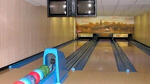 A bowling alley with multiple lanes, a bowling ball return, and two televisions mounted on the wall.