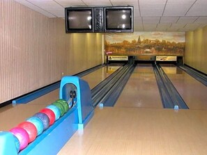 A bowling alley with multiple lanes, a bowling ball return, and two televisions mounted on the wall.