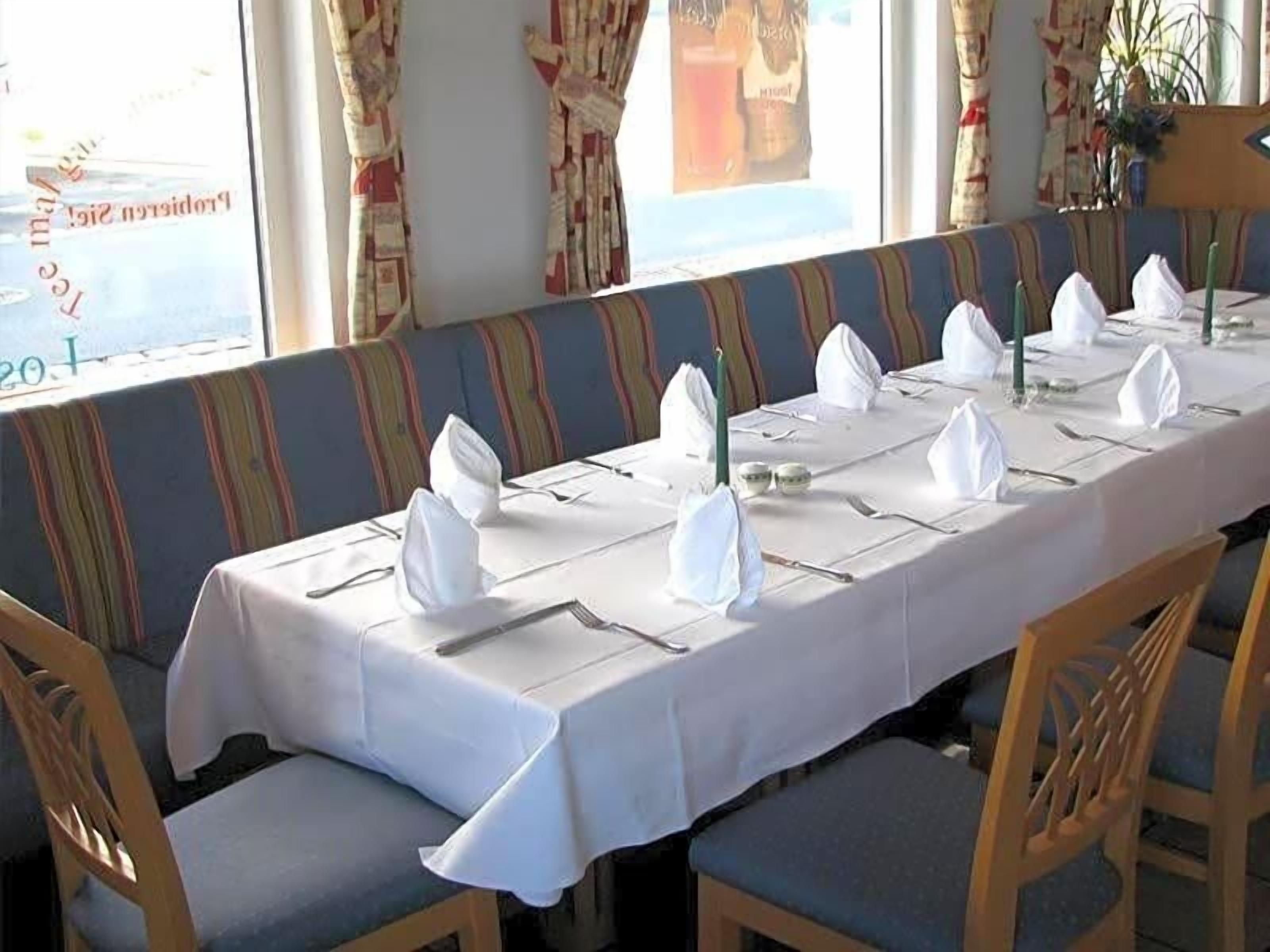 Un coin repas avec une longue table dressée pour le repas, des bancs rembourrés et une fenêtre avec des rideaux.