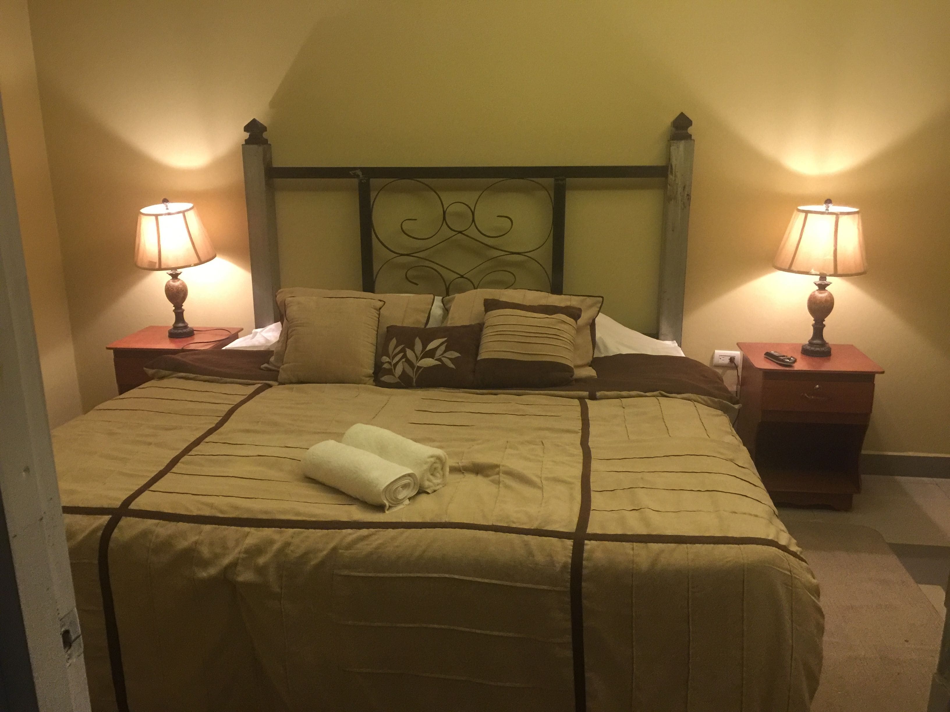A neatly made bed with a brown bedspread, two bedside lamps, and a headboard with a decorative design.